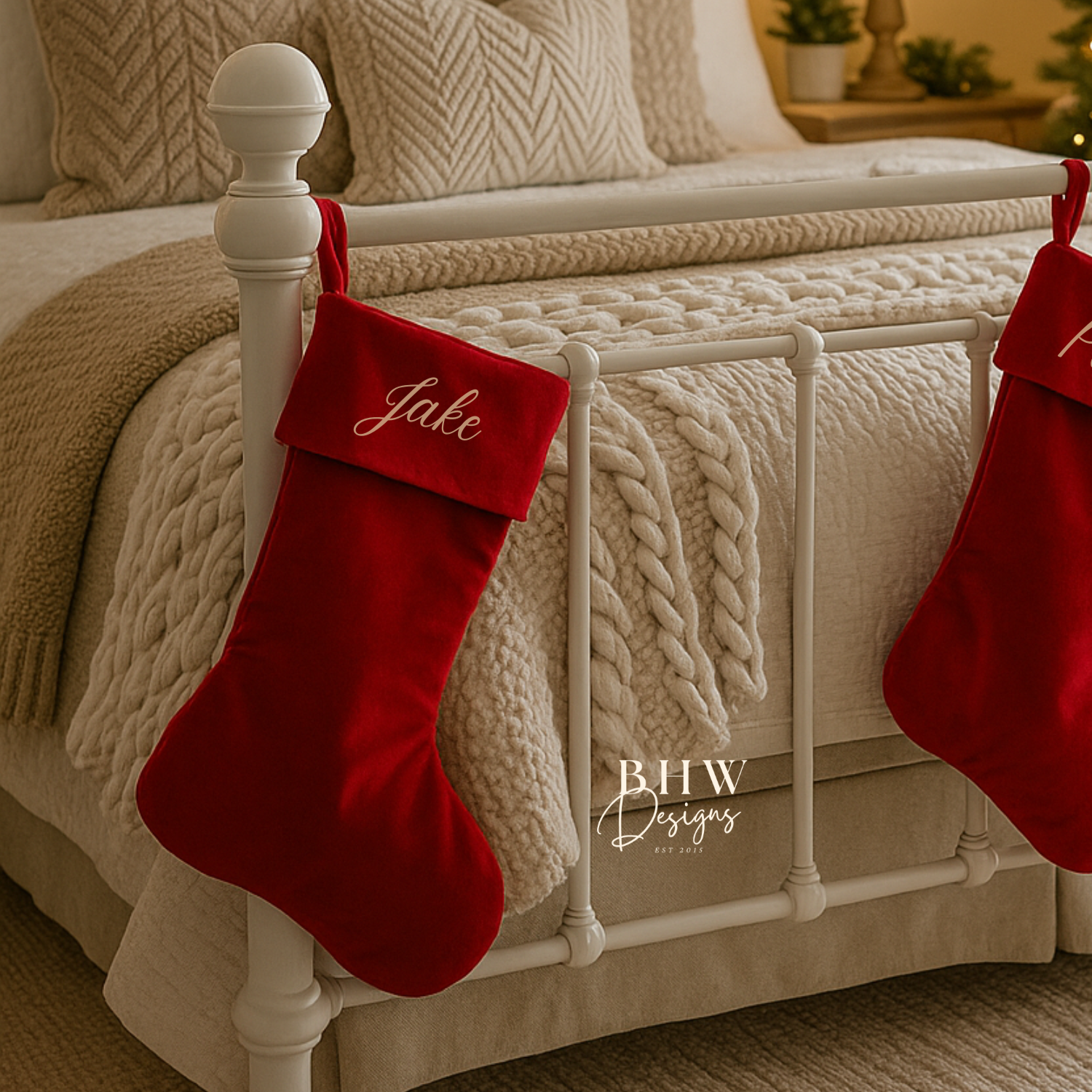 Red Christmas stockings with 'Jake' personalised on a bed with beige bedding and white posts.