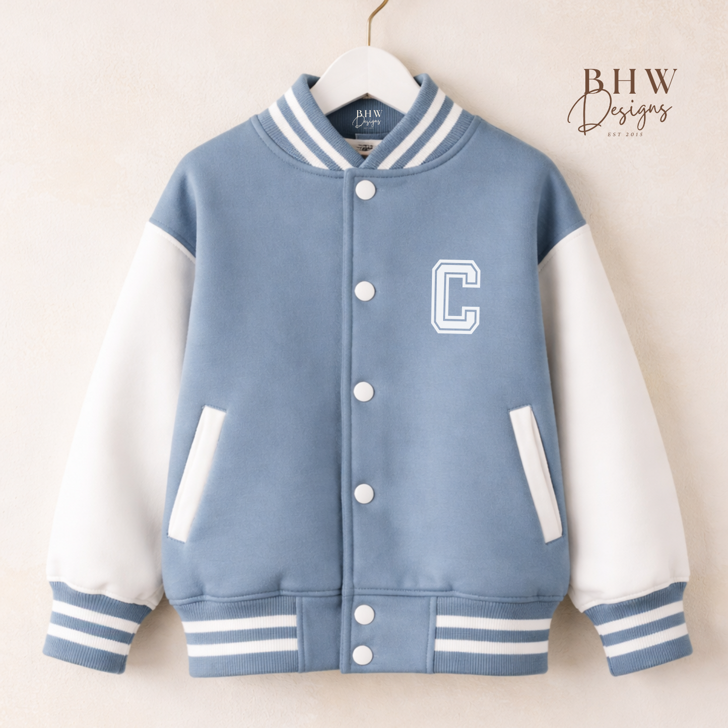 Blue and white varsity jacket with a letter 'C' on a hanger against a beige background