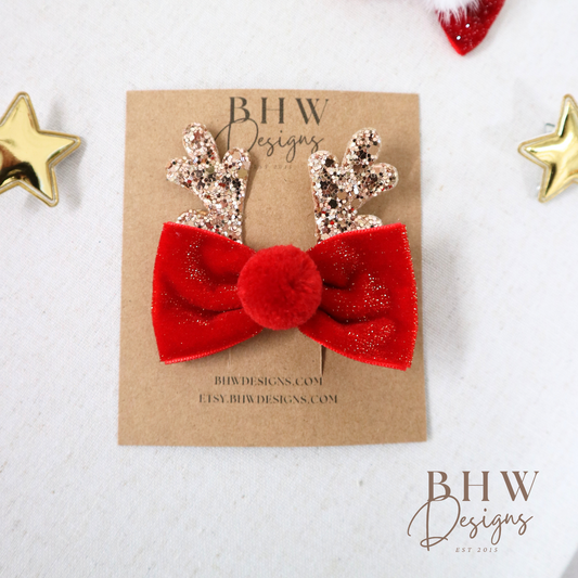 Red bow hair clip with gold antlers on a BHW Designs branded card.