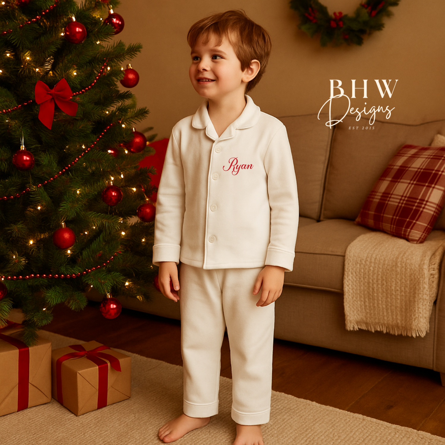Child in personalised white pyjamas standing in a cozy living room with a Christmas tree and presents.