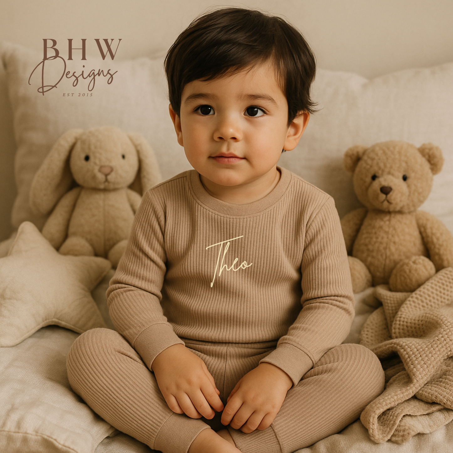 Child wearing a beige ribbed outfit with 'Theo' printed on it, sitting on a bed 