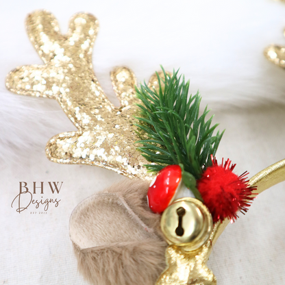 Decorative headband with gold antlers, greenery, red accents, and a gold bell on a white background. Brand 'BHW Designs' visible.