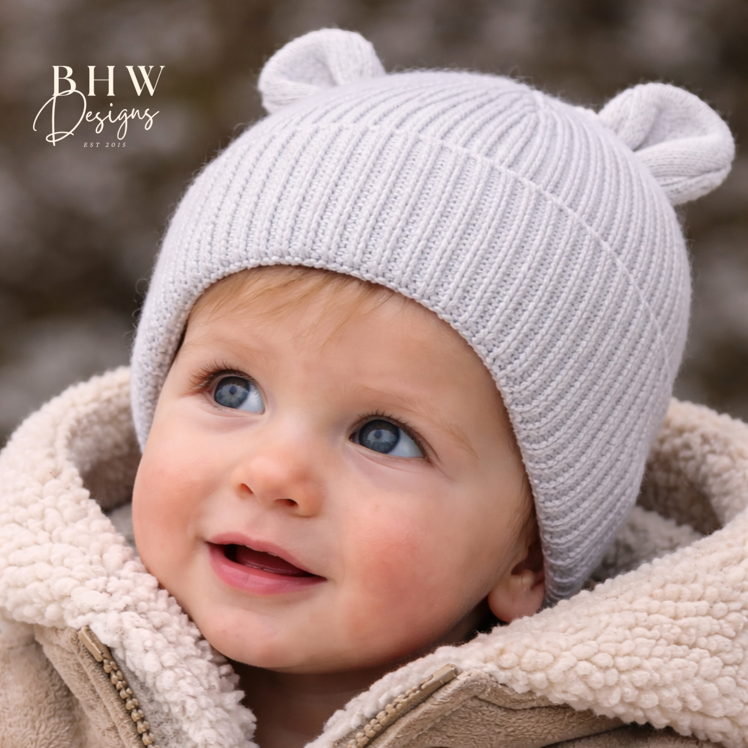 Baby wearing a light grey knit hat with bear ears and a beige fleece jacket.
