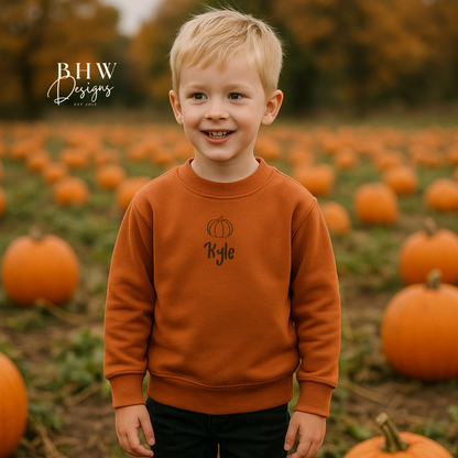 Child wearing a rust orange sweatshirt with 'Kyle' on it, standing in a pumpkin field.