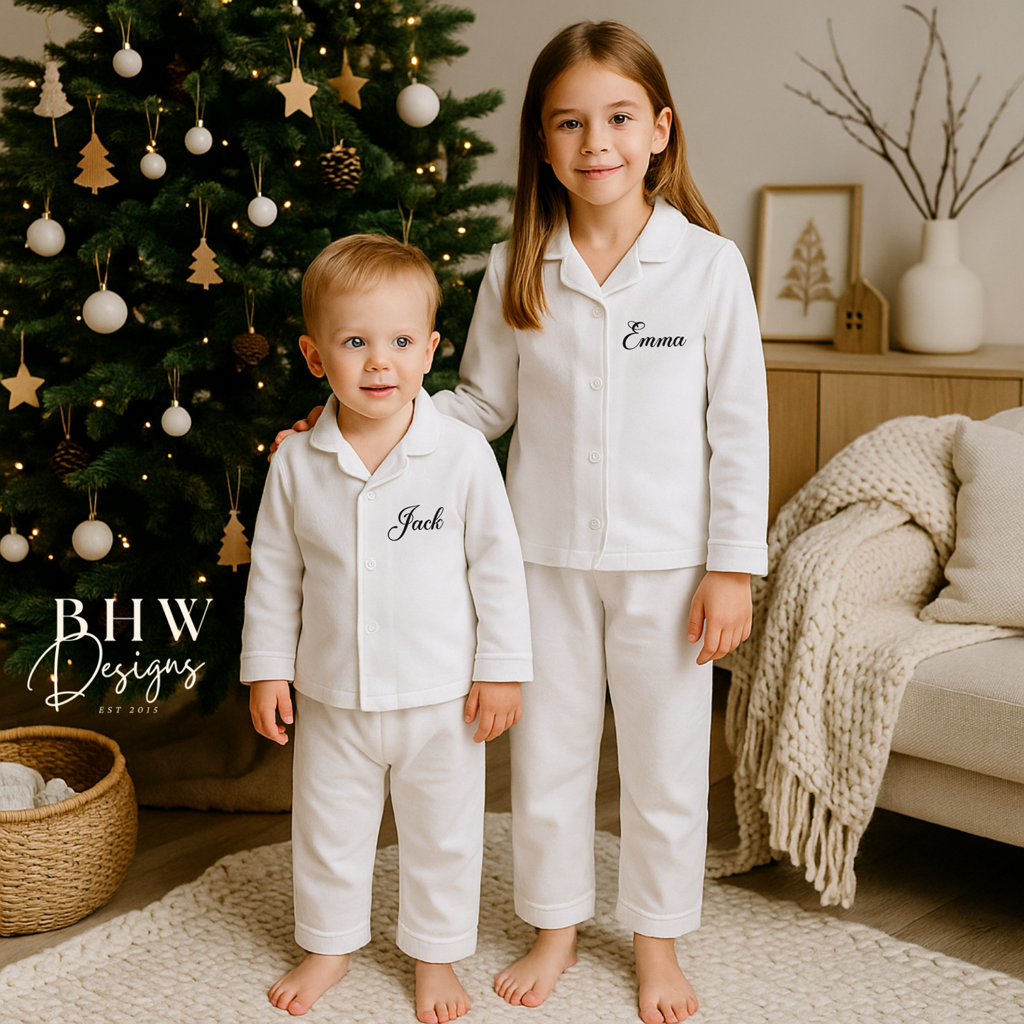 Two children in matching white pajamas standing in front of a decorated Christmas tree.