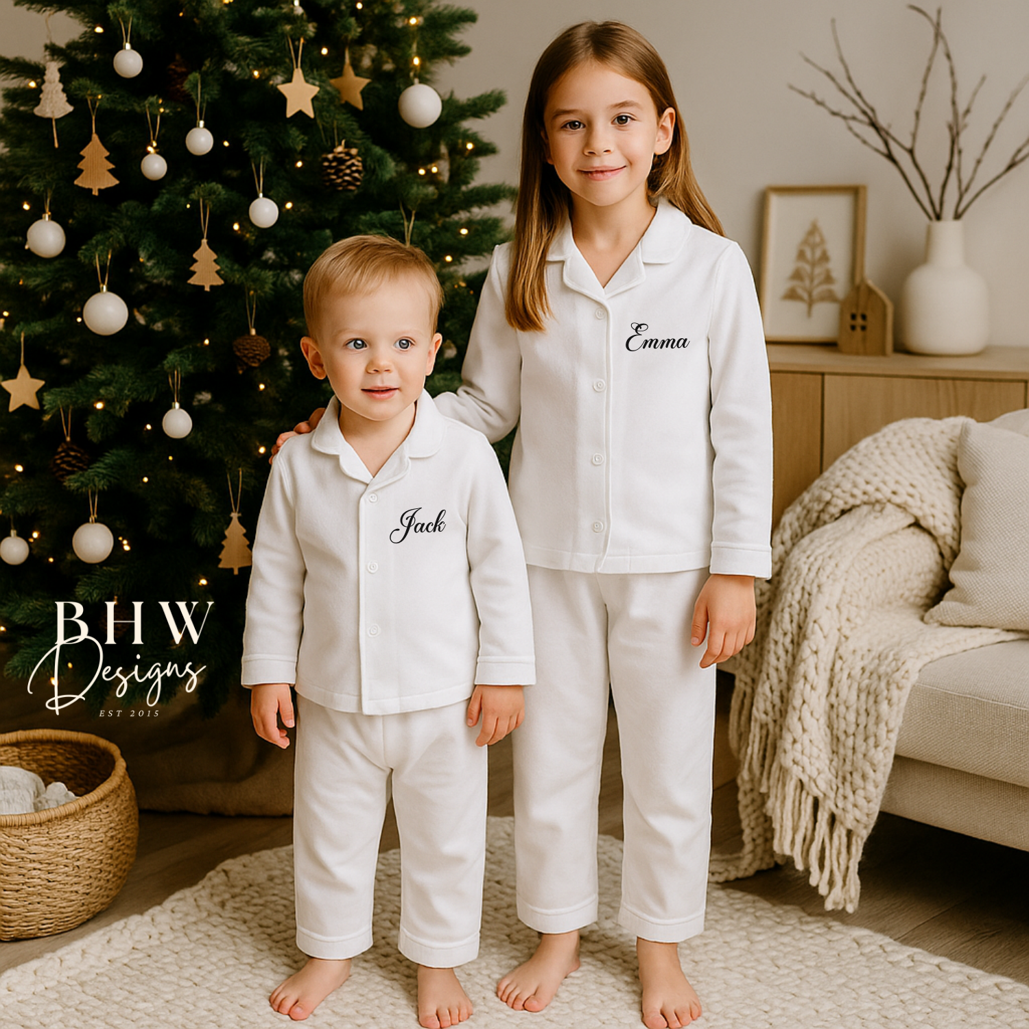 Two children in matching white pajamas standing in front of a decorated Christmas tree.