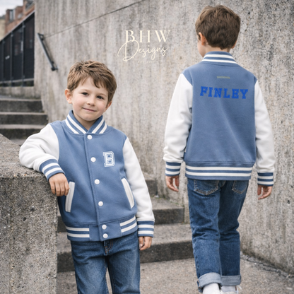 Two children wearing matching dusky blue and white varsity jackets with 'FINLEY' on the back, standing on a concrete staircase.