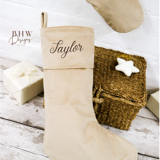 Beige Christmas stocking with 'Taylor' personalised on it, placed on a wooden surface.