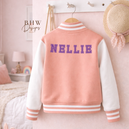 Peach Pink varsity jacket with 'NELLIE' on the back in purple in a bedroom setting