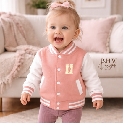 Child wearing a peach pink varsity jacket with a yellow 'H' in a living room setting.