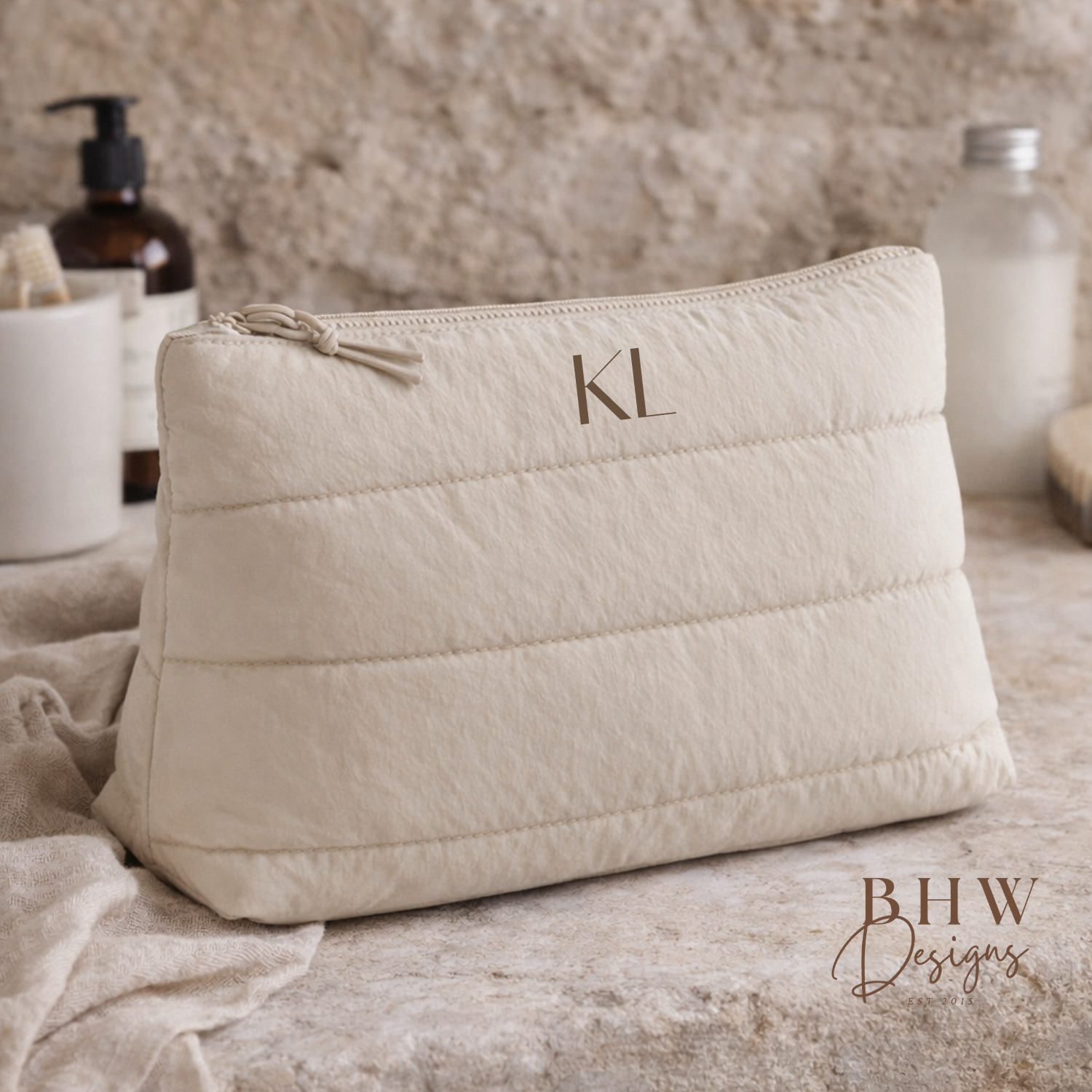 Beige quilted pouch with initials on a textured surface,