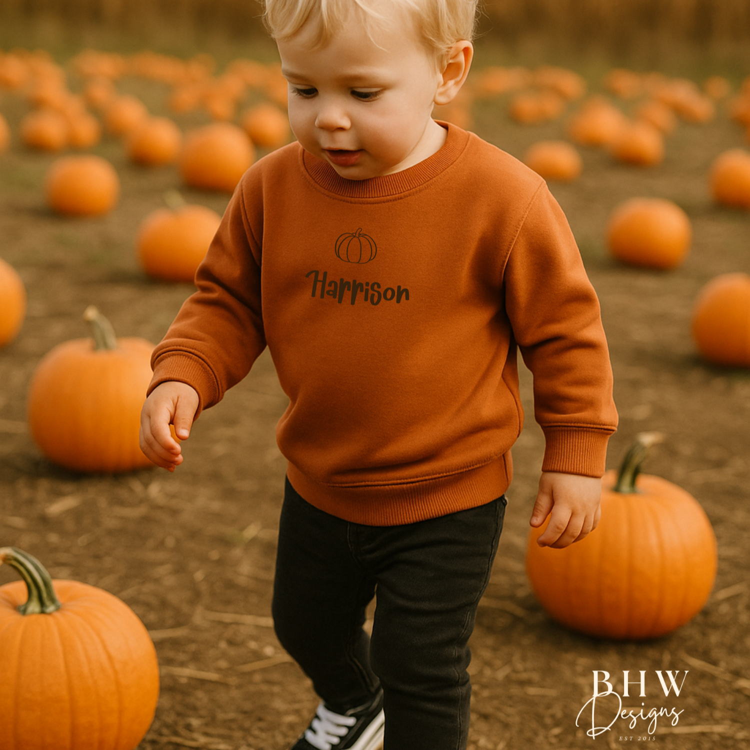 Child in a rust orange sweater standing in a pumpkin patch with a pumpkin print and personalised with Harrison