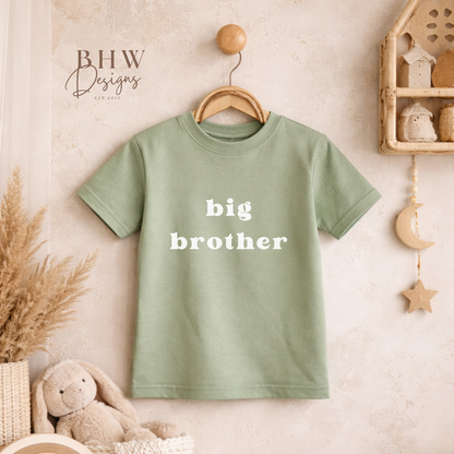 Green t-shirt with 'big brother' text hanging on a wooden hanger in a nursery setting.