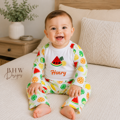 Baby wearing a colourful fruit-themed pyjamas sitting on a bed.