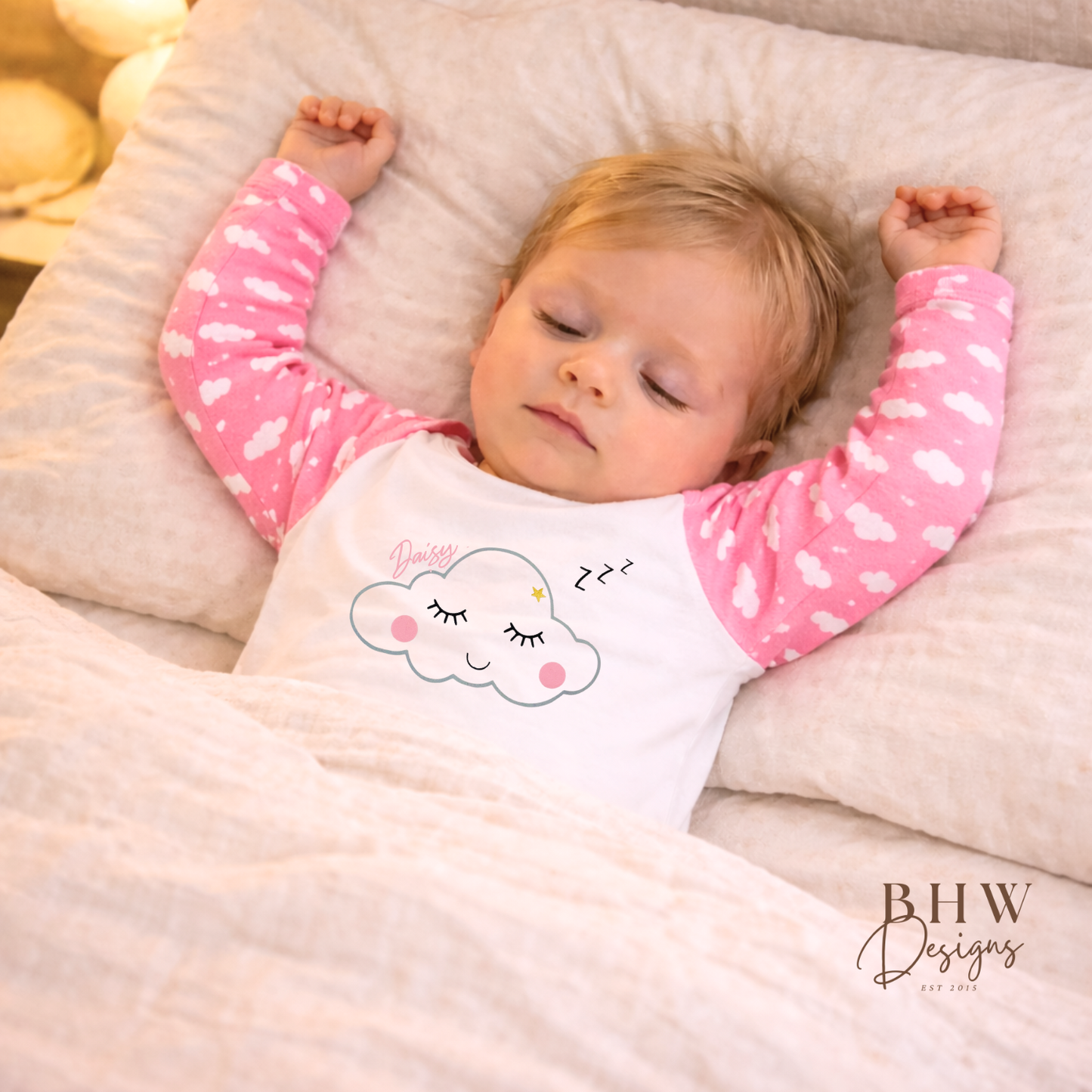 Baby sleeping in a bed with pink and white pyjamas featuring a cloud design.