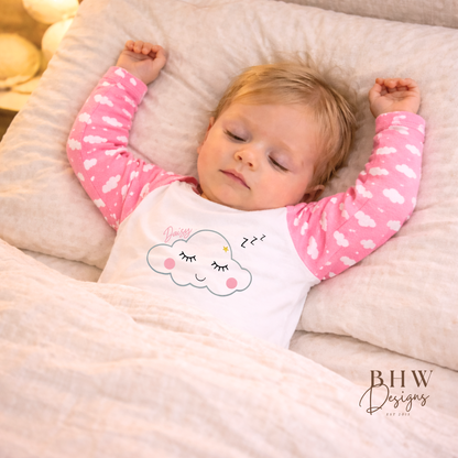 Baby sleeping in a bed with pink and white pyjamas featuring a cloud design.