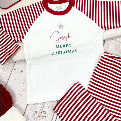 Children's red and white striped pajama set with 'Merry Christmas' text on a wooden surface.