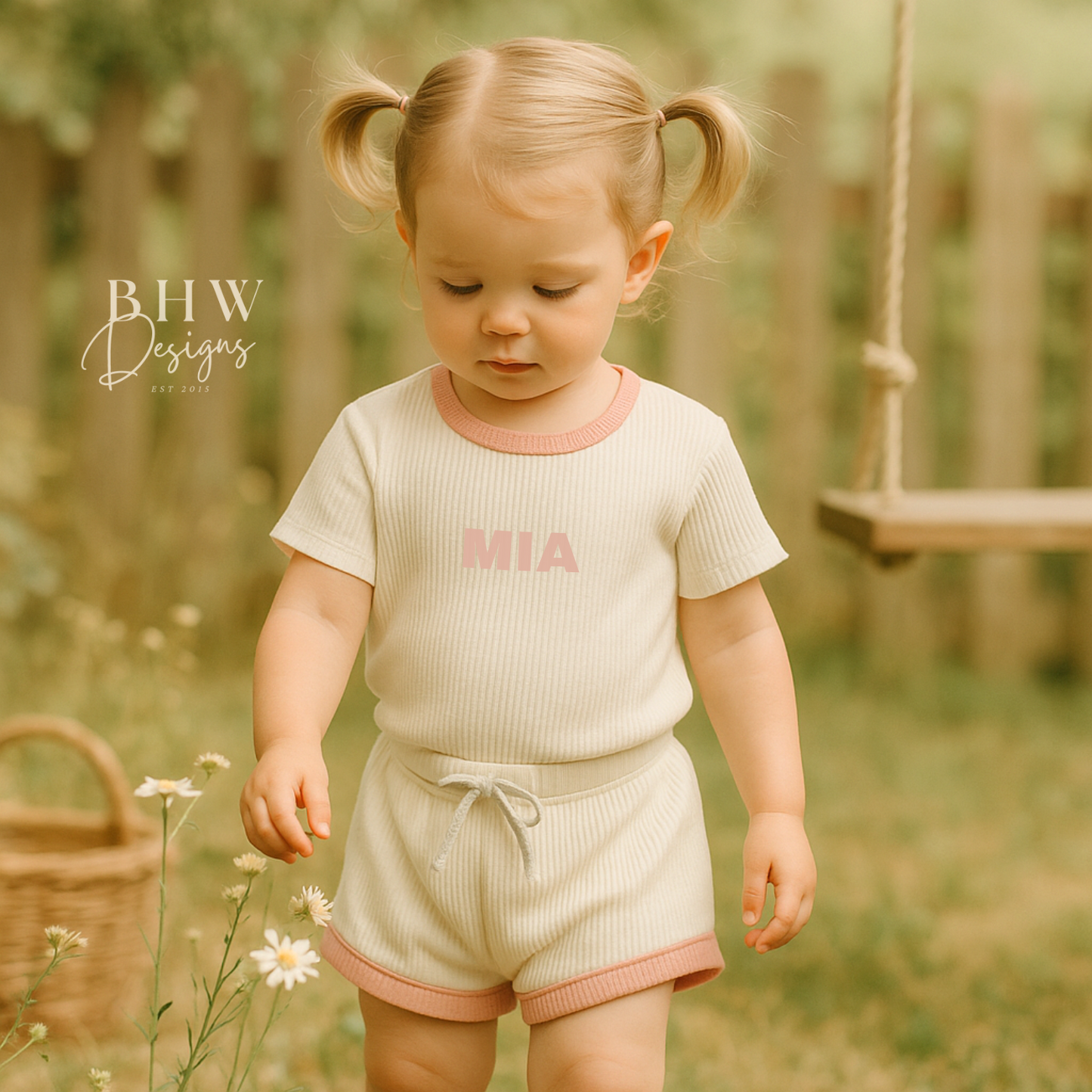Girl wearing a white ribbed t shirt and short set with 'MIA' printed on the front in baby pink