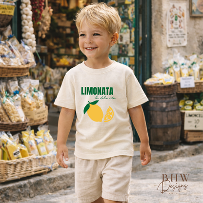 Child wearing a 'Limonata' t-shirt with lemons in an outdoor market setting