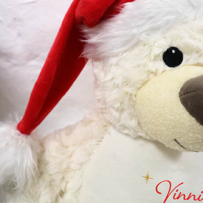 Cream teddy bear wearing a red Santa hat on a white background with 'Vinnie's First' text.