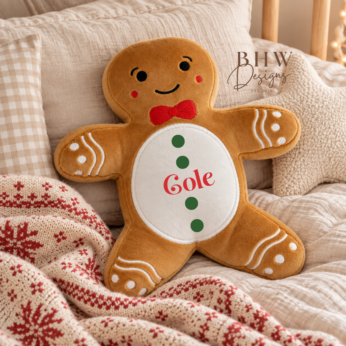 A gingerbread man plush pillow with 'Gole' embroidered on the belly, styled on a cozy bed with a knit holiday blanket. The brand logo 'BHW Designs' is visible in the upper right.