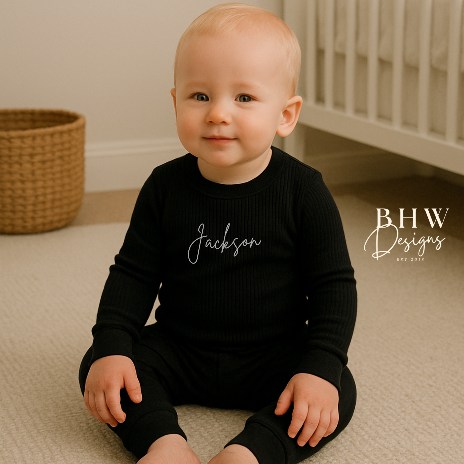 Baby wearing a ribbed black outfit with 'Jackson' printed on it, sitting on a beige carpet.