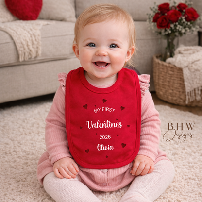 Baby wearing a red 'My First Valentine's 2026' bib sitting on a carpeted floor.