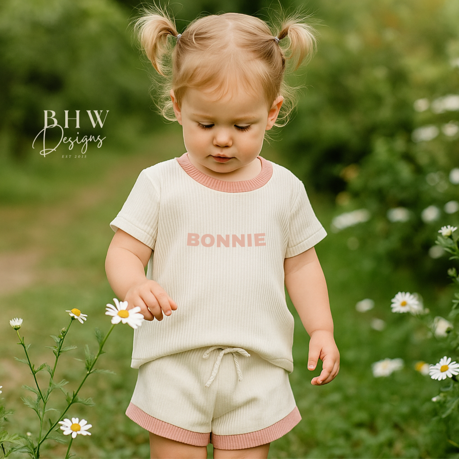 Child wearing a white ribbed outfit with 'Bonnie' on the front in baby pink. 