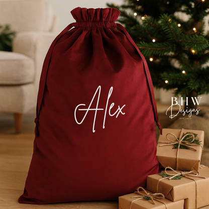 Red drawstring bag with 'Alex' on it, surrounded by small gift boxes and a Christmas tree.