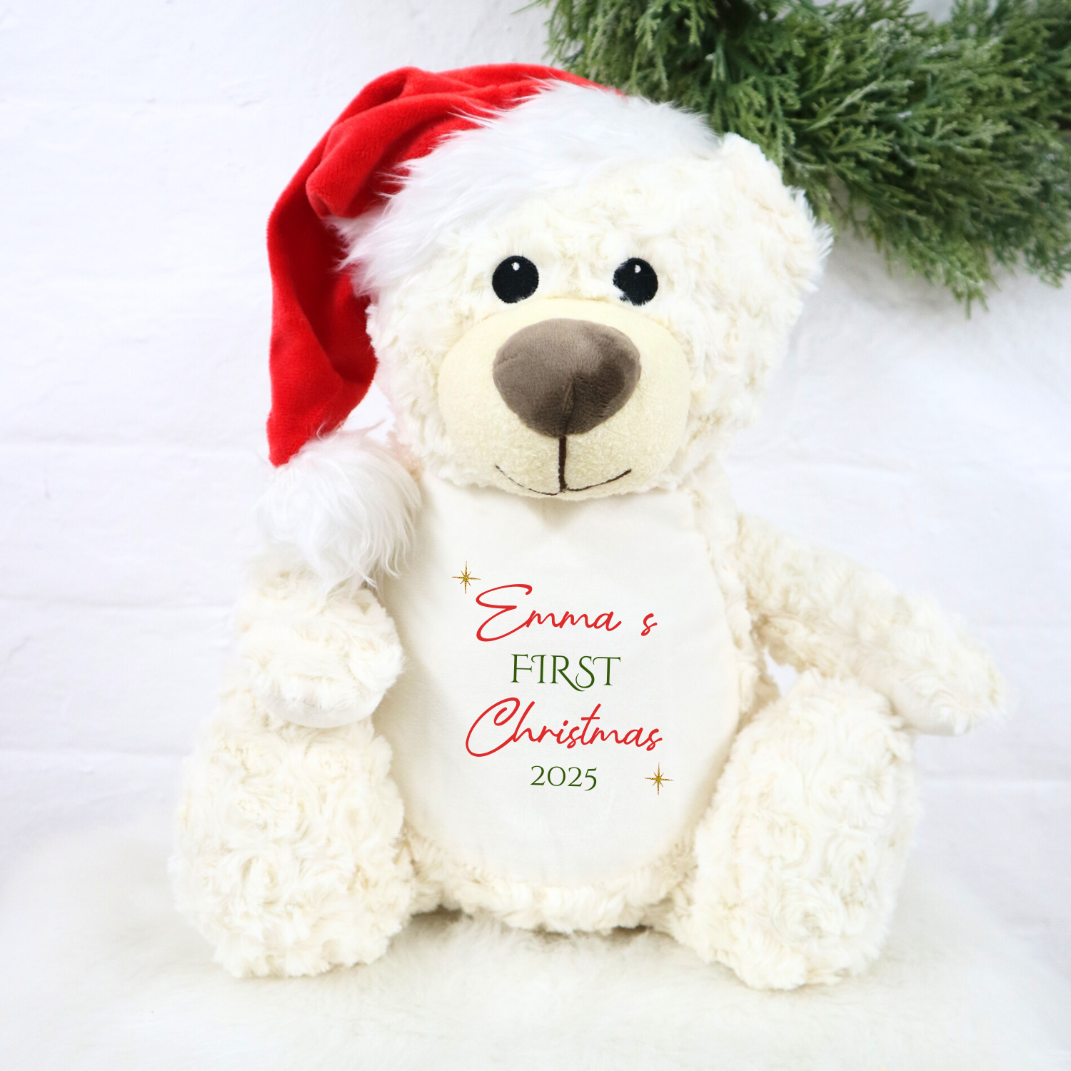White teddy bear wearing a red Santa hat with 'Emma's First Christmas 2025' text on a white background.