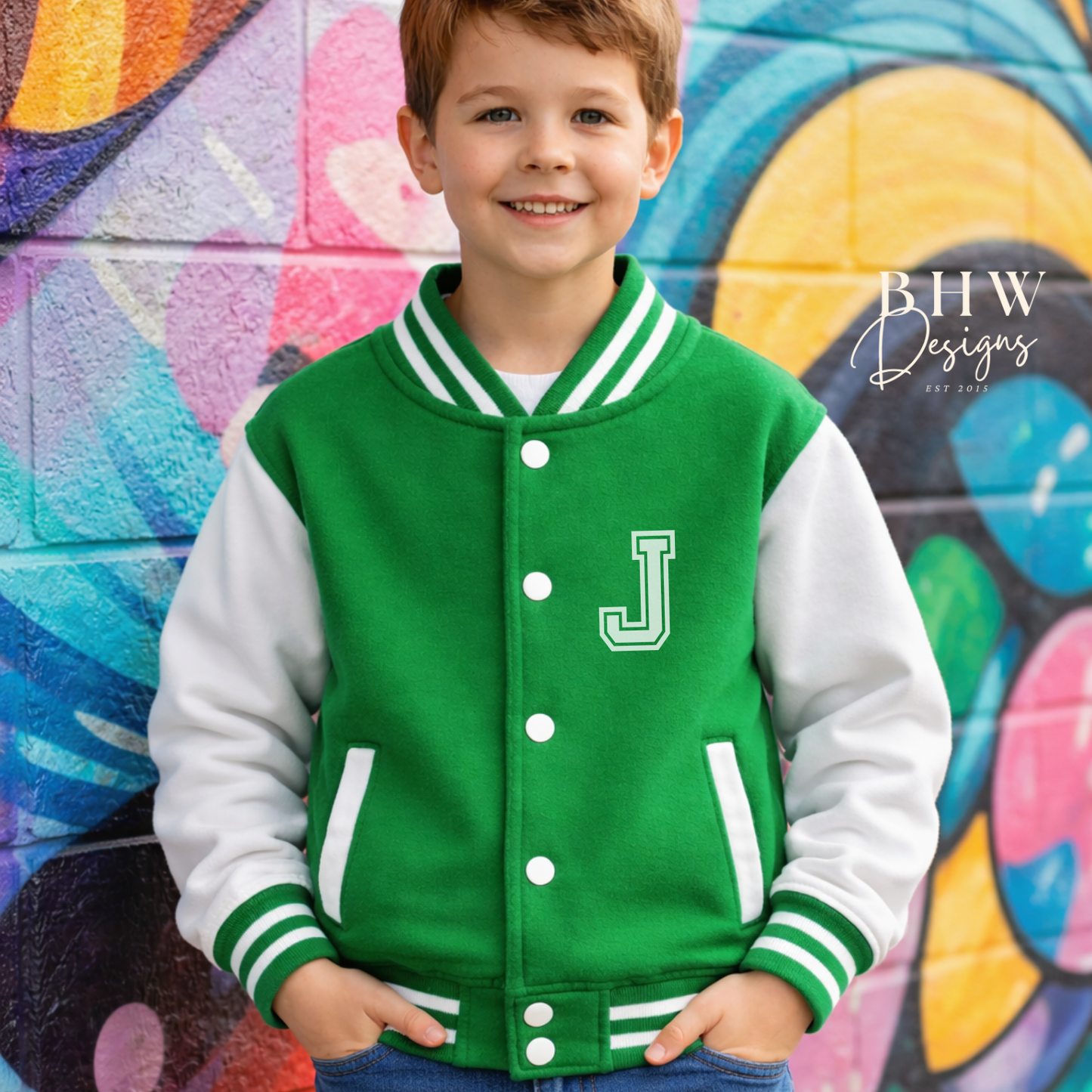 Child wearing a green varsity jacket with a letter 'J' in front of a colorful mural.