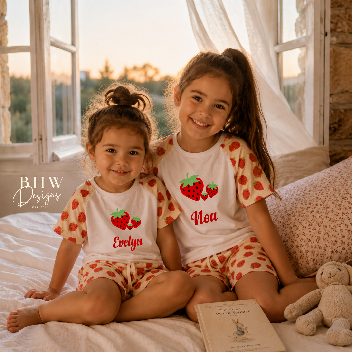 Two children wearing matching pajamas with strawberry designs sitting on a bed.
