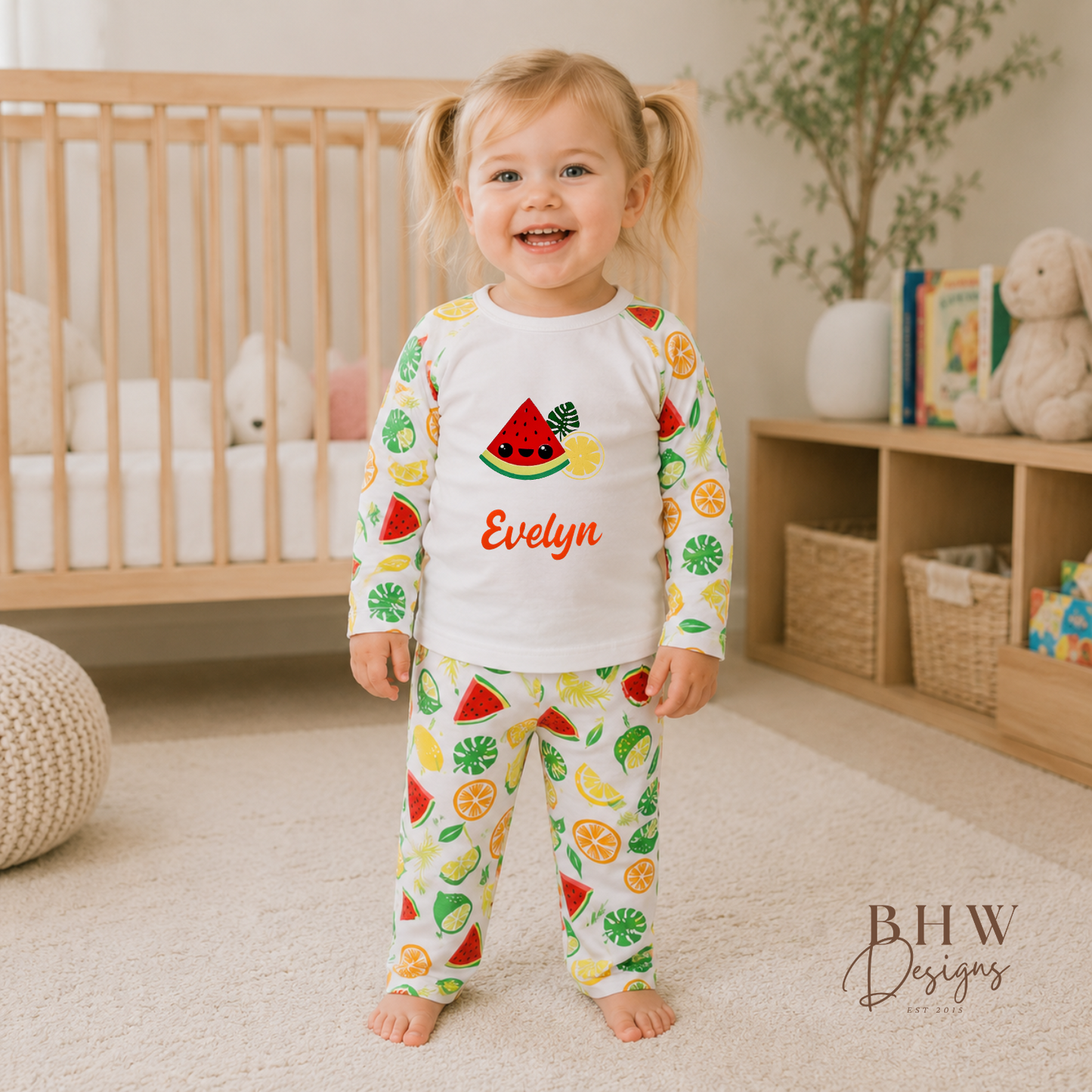Child wearing colorful pajamas with fruit design in a nursery setting, standing in front of a crib.