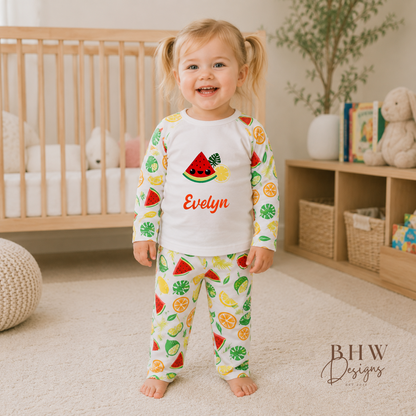 Child wearing colorful pajamas with fruit design in a nursery setting, standing in front of a crib.