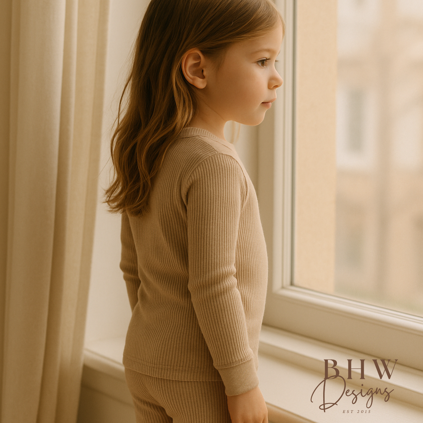 Young girl in beige ribbed outfit standing by a window, 