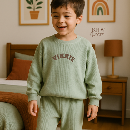 Child wearing a green 'Vinnie' sweater and pants in a bedroom setting