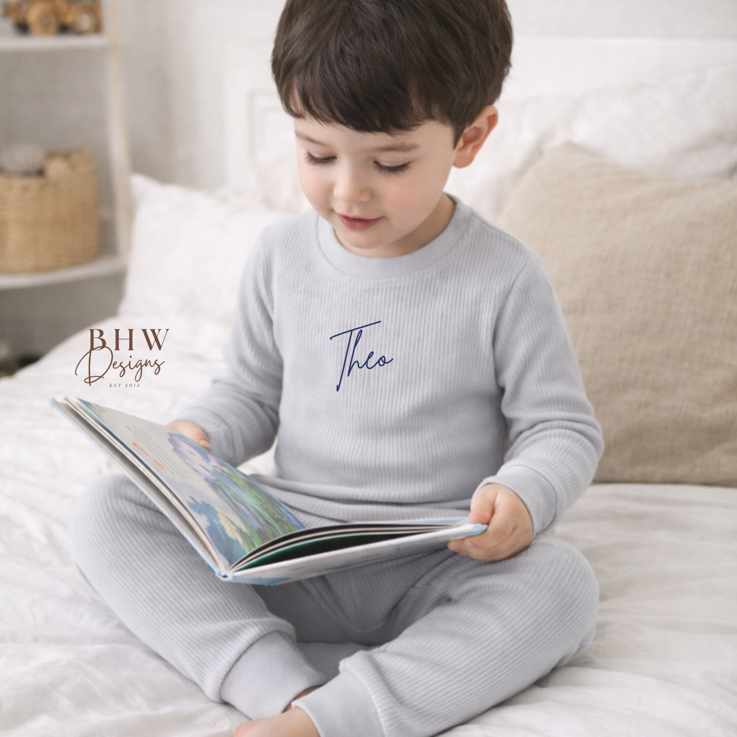 Child in a personalised light grey lounge set reading a book on a bed