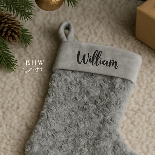 Grey textured Christmas stocking with 'William' on a beige surface with festive decorations.