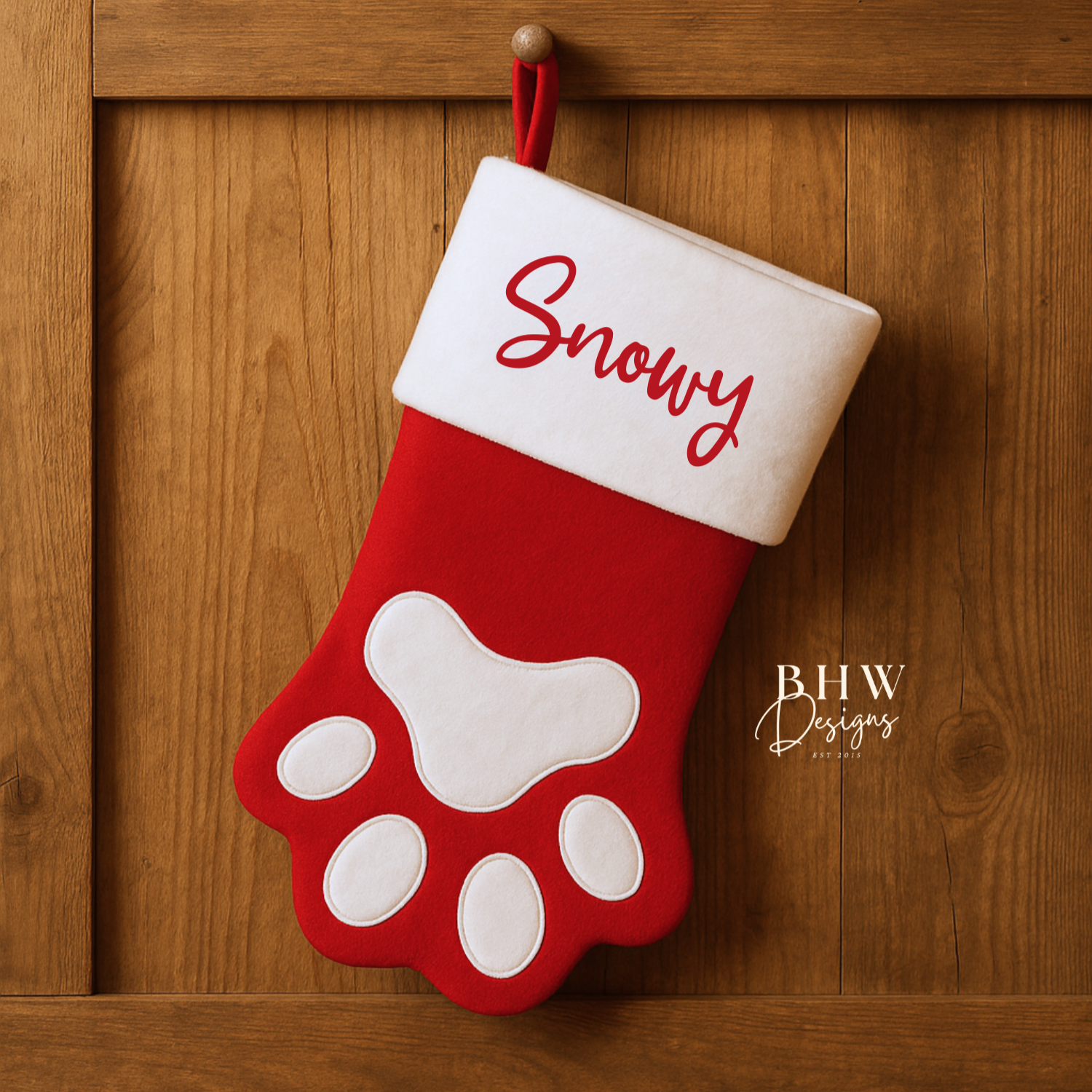Red and white Christmas stocking with paw design and 'Snowy' text, hanging on a wooden door.