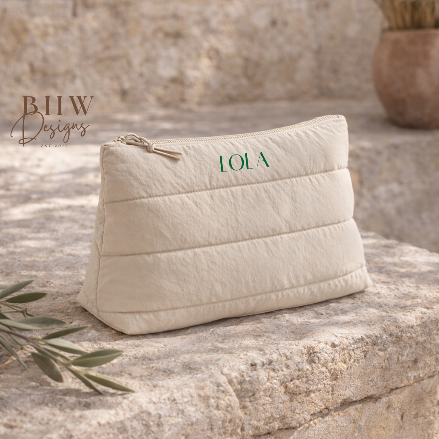 beige quilted pouch with 'LOLA' on the front on a stone surface,