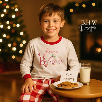 Child wearing personalised white and red checked pyjamas with cookies and milk for Santa, sitting at a table with a blurred Christmas tree in the background.