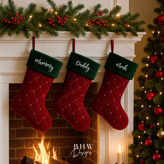 Three red personalised Christmas stockings with green trim hanging above a fireplace, decorated with lights and a tree.
