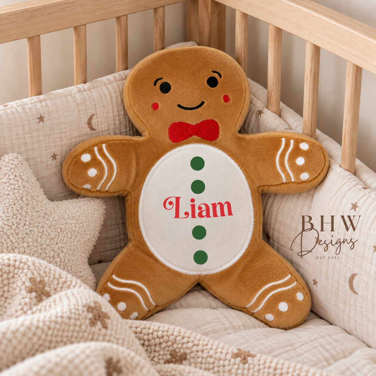 A gingerbread man plush pillow with the name 'Liam' personalized on the belly, resting inside a wooden crib with beige bedding.