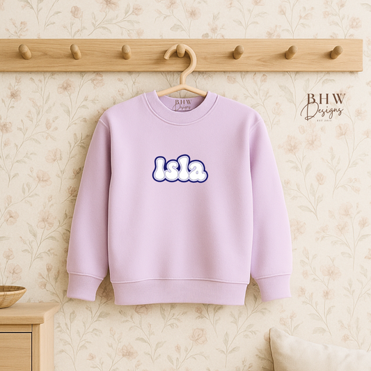 Lilac sweatshirt with 'lala' text on a hanger against a neutral wall.