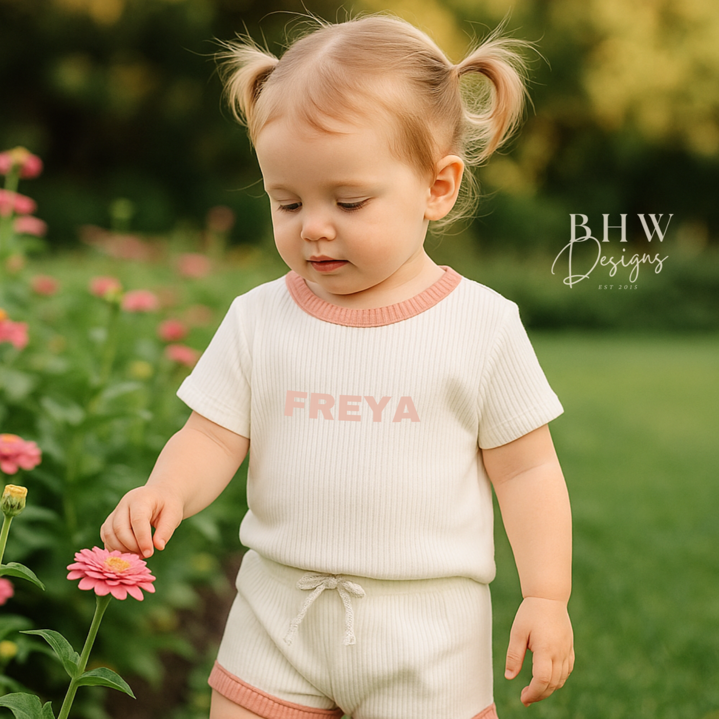 Child wearing a white ribbed outfit with baby pink trim and 'FREYA' printed on the front in baby pink. 
