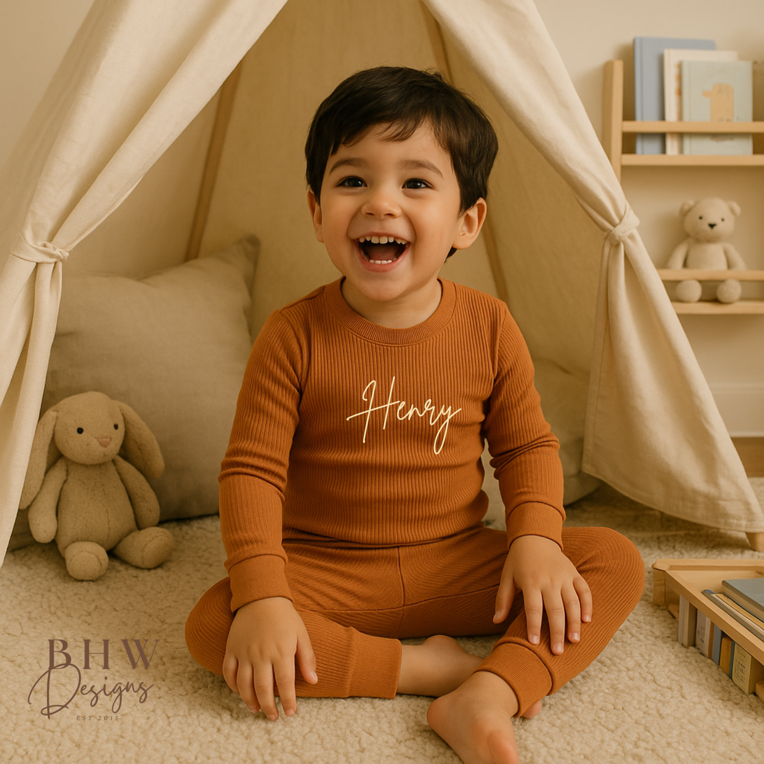 Child wearing a rust outfit with 'Henry' printed on it, sitting inside a cozy tent-like structure.