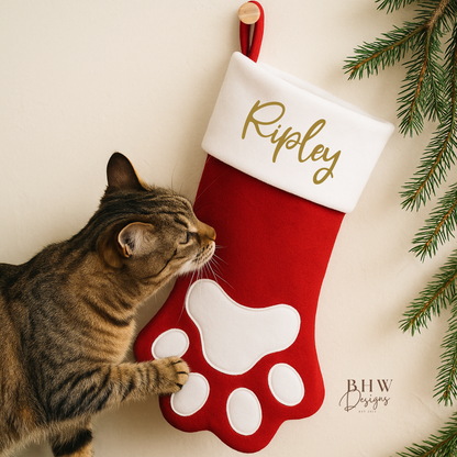 Cat interacting with a red and white Christmas stocking in a paw shape design personalised with Ripley in Gold