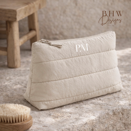Beige quilted pouch with initials on a stone surface, next to a wooden stool.