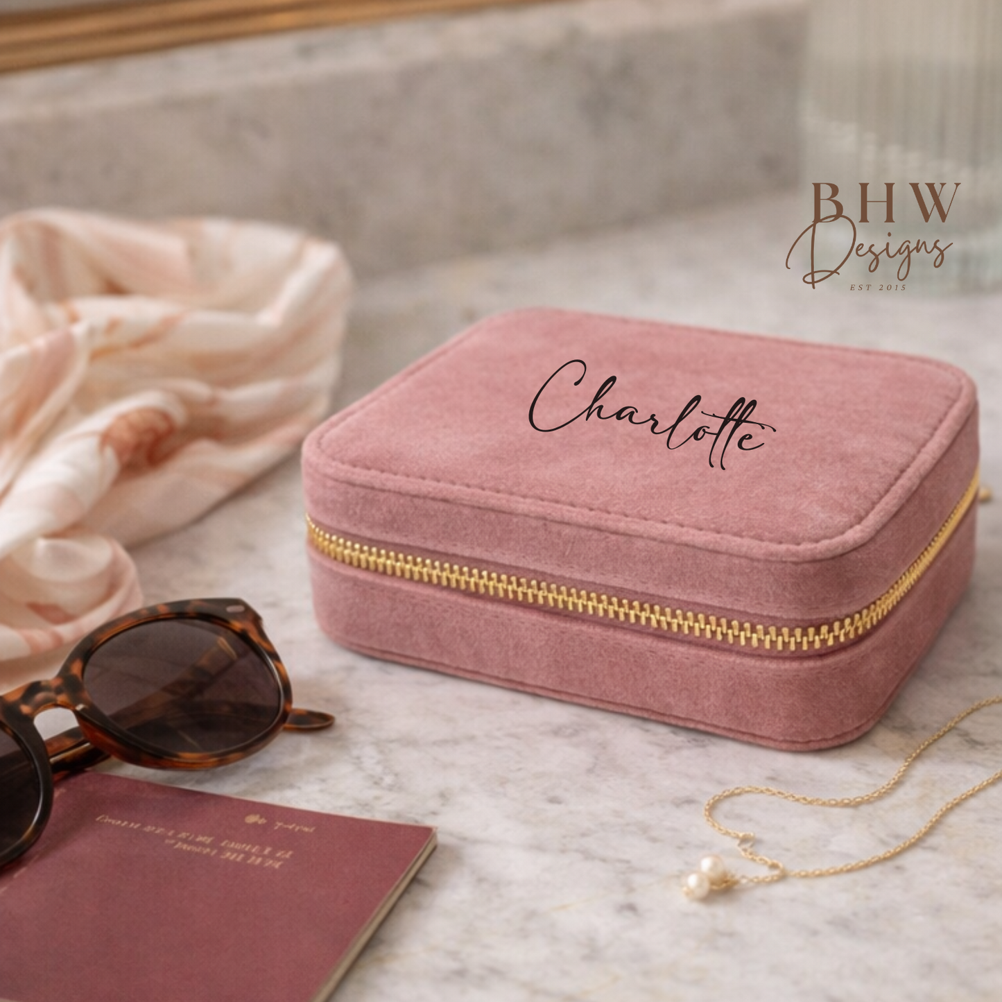 Pink jewellery box with 'Charlotte' on a marble surface with sunglasses 