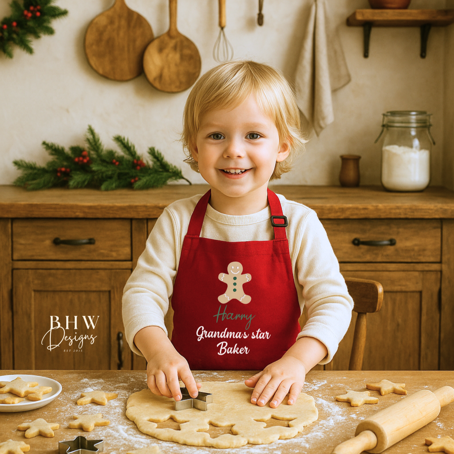 Child in a red apron with a gingerbread man design, cutting out cookies from dough in a kitchen.